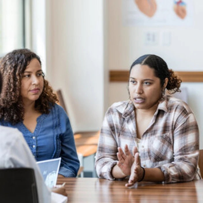 Deux femmes discutent avec une professionnelle dans un bureau lors d’une rencontre de conseil d’école.